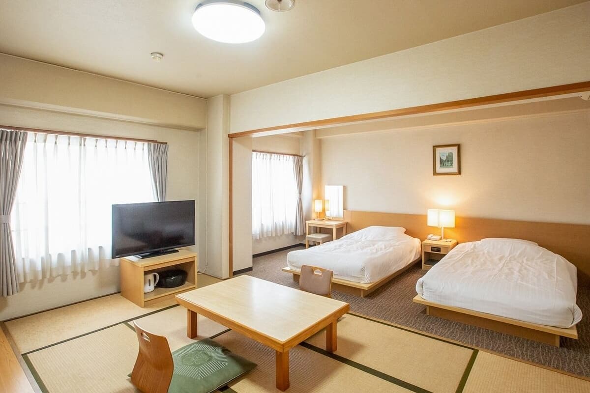 A hotel room with a TV, two beds, a table, and a sofa.