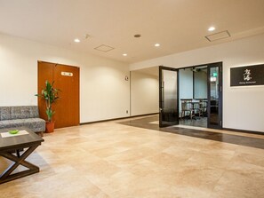 A modern interior with a reception desk, a sofa, a potted plant, and a dining area visible through a glass door. - Hotel Sunplaza Sakai (Sakai)