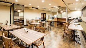 Un restaurant spacieux avec de nombreuses tables et chaises en bois, un espace cuisine à l’arrière-plan et un coin salon avec un comptoir.