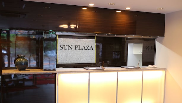 Un comptoir d’accueil avec une enseigne indiquant « SUN PLAZA » et un vase placé à gauche.