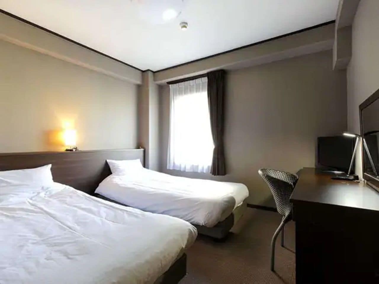 A hotel room with two beds, a desk, a chair, a television, and a window with curtains.