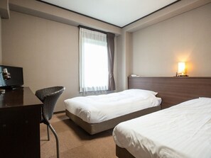 Habitación de hotel con dos camas individuales, un escritorio con silla, televisión y ventana con cortinas.