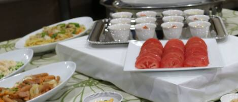 A buffet table with various dishes, including a plate of sliced tomatoes, several bowls of food, and a tray with small dishes.
