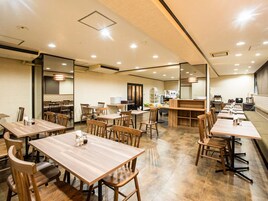 Ein geräumiges Restaurant mit mehreren Holztischen und -stühlen, einem Küchenbereich im Hintergrund und einer Sitzgelegenheit mit einer Theke.