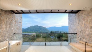 A modern bathroom with a bathtub, a glass-enclosed balcony with a view of mountains. - Botanica Khao Yai (Pak Chong)