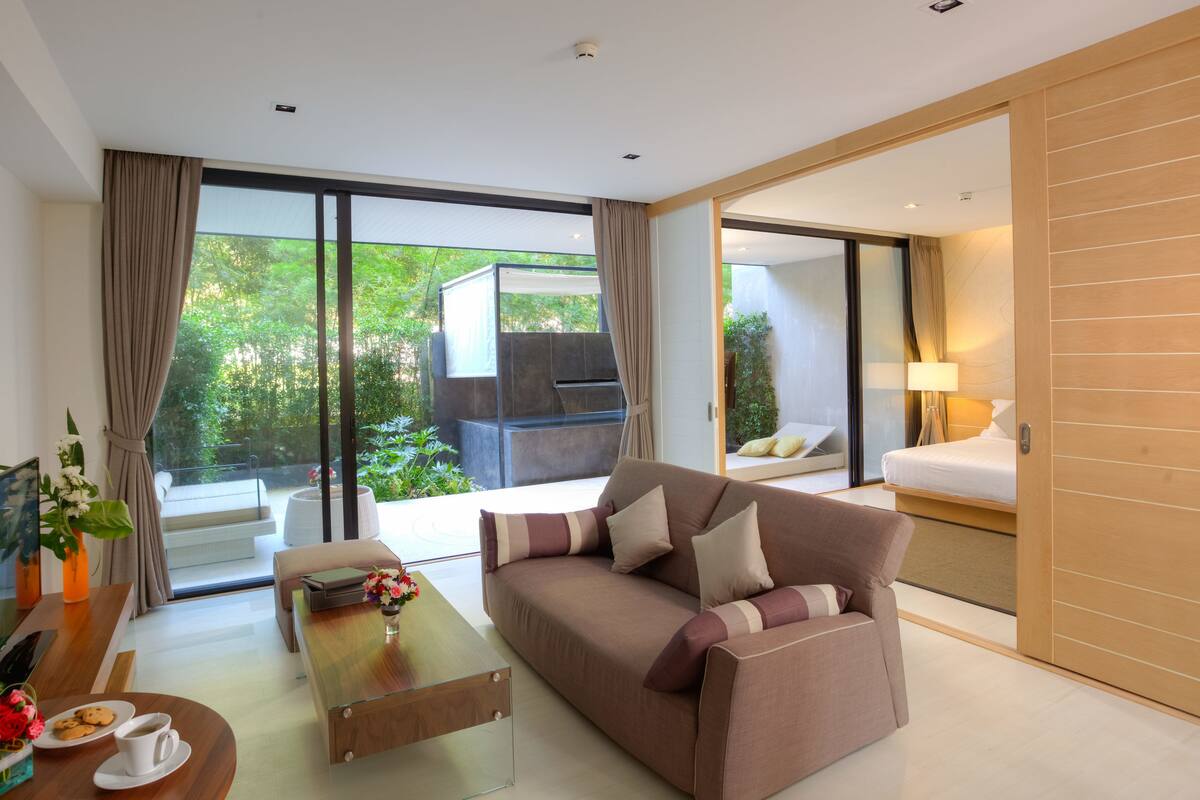 A modern hotel room with a sofa, a coffee table, a TV, and a balcony with a grill.