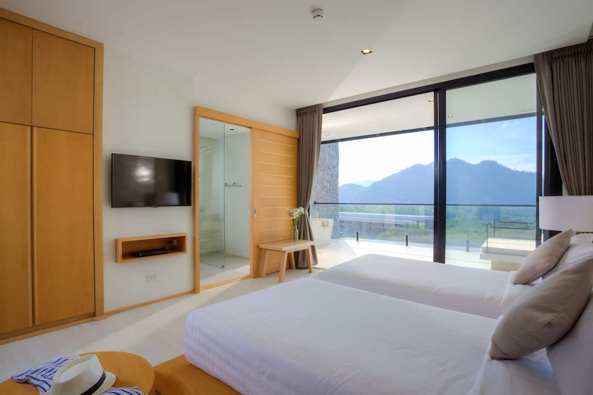 A modern hotel room with a large bed, a television, a wooden wardrobe, and a balcony with a mountain view.
