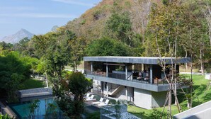 A modern building with a pool, surrounded by lush greenery and a mountain in the background. - Botanica Khao Yai (Pak Chong)