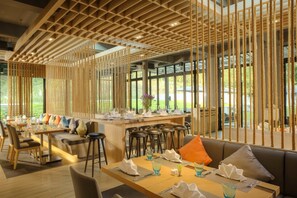 Un restaurante moderno con separadores de madera, una zona de bar y un espacio de estar con mesas y un sofá.
