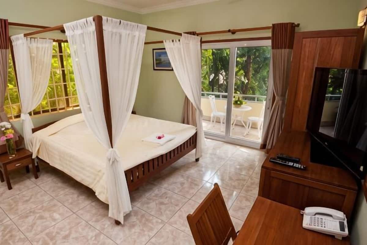 A four-poster bed with curtains, a TV, a desk with a phone, and a balcony with chairs.