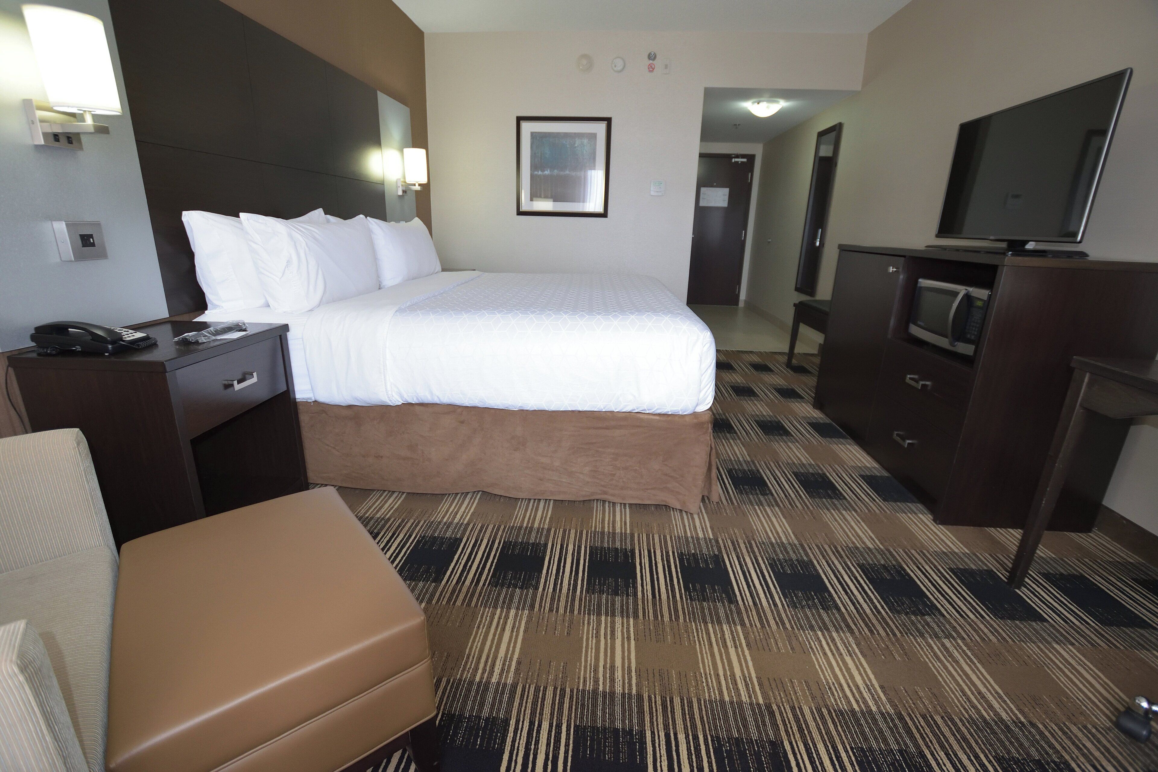 A hotel room with a bed, a desk with a telephone, a television, and a seating area.