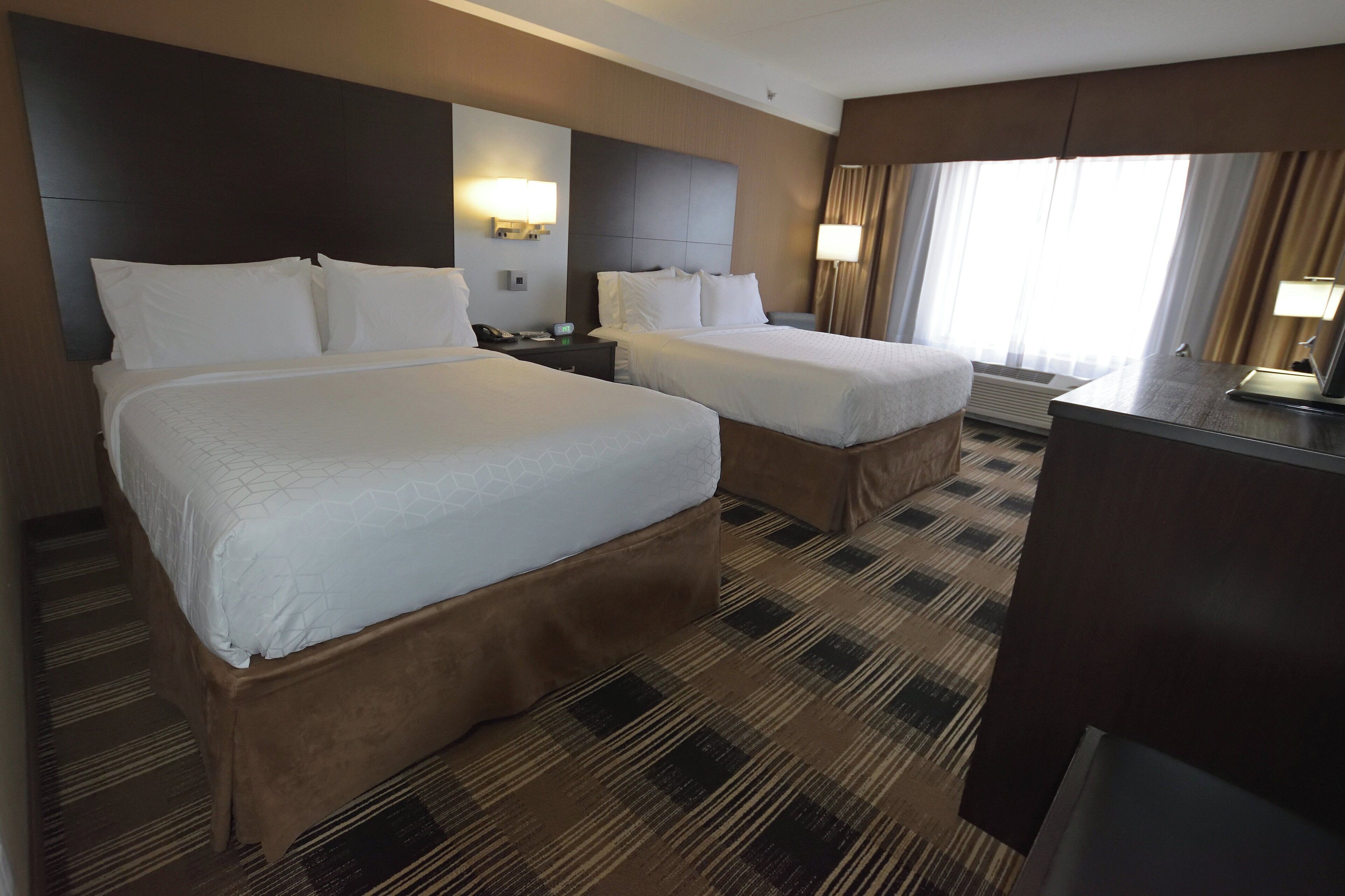 Habitación de hotel con dos camas, un escritorio y un gran ventanal con cortinas.