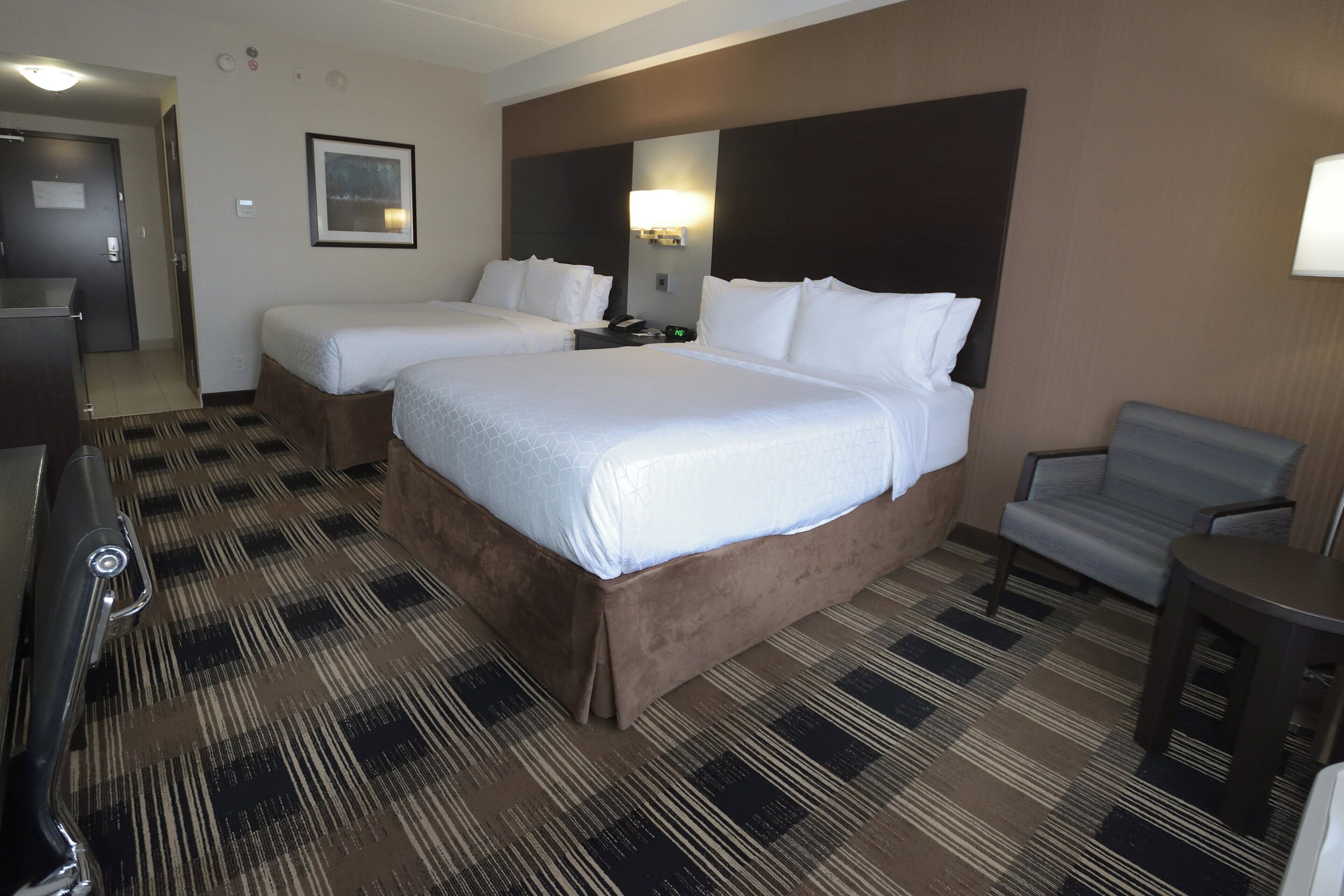 A hotel room with two beds, a desk, a chair, and a patterned carpet.