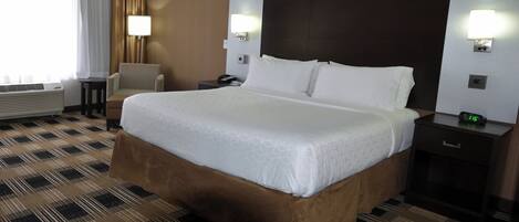 A hotel room with a large bed, a chair, a bedside table, a lamp, and a clock.