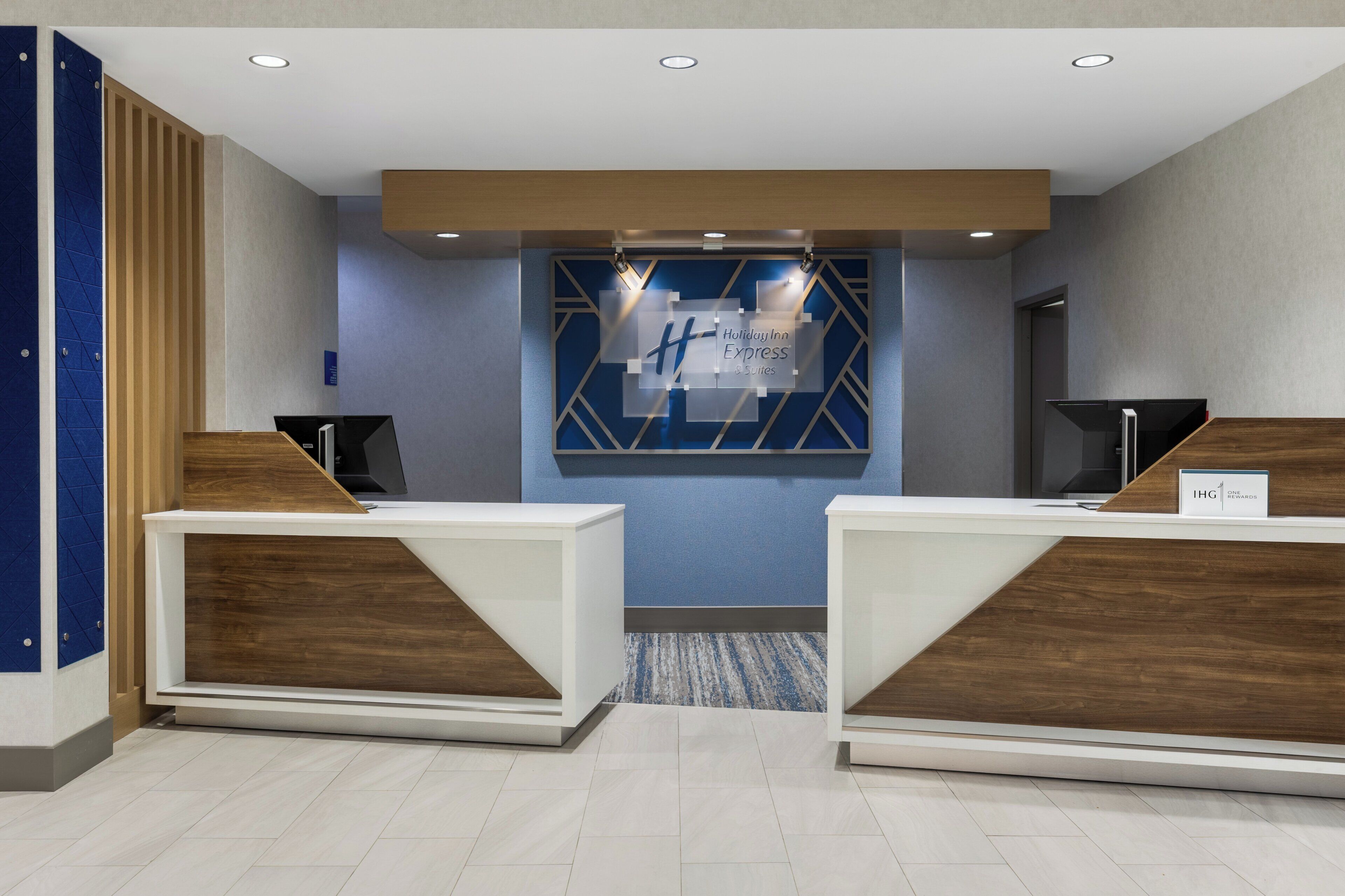 Zona de recepción con dos mostradores, pared de acento azul y cartel de Holiday Inn Express & Suites.