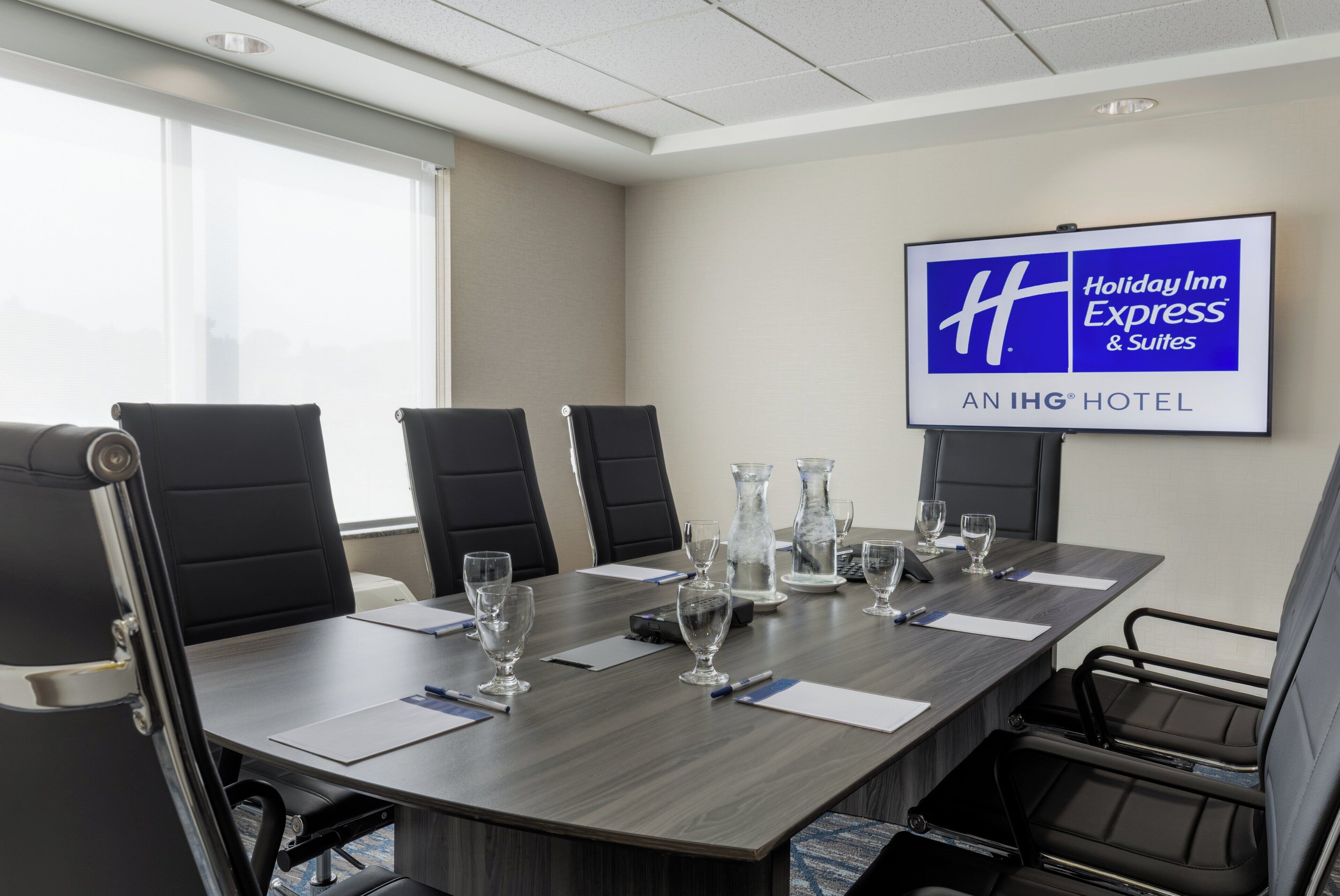 A conference room with a large table, black chairs, and a screen displaying the Holiday Inn Express logo.