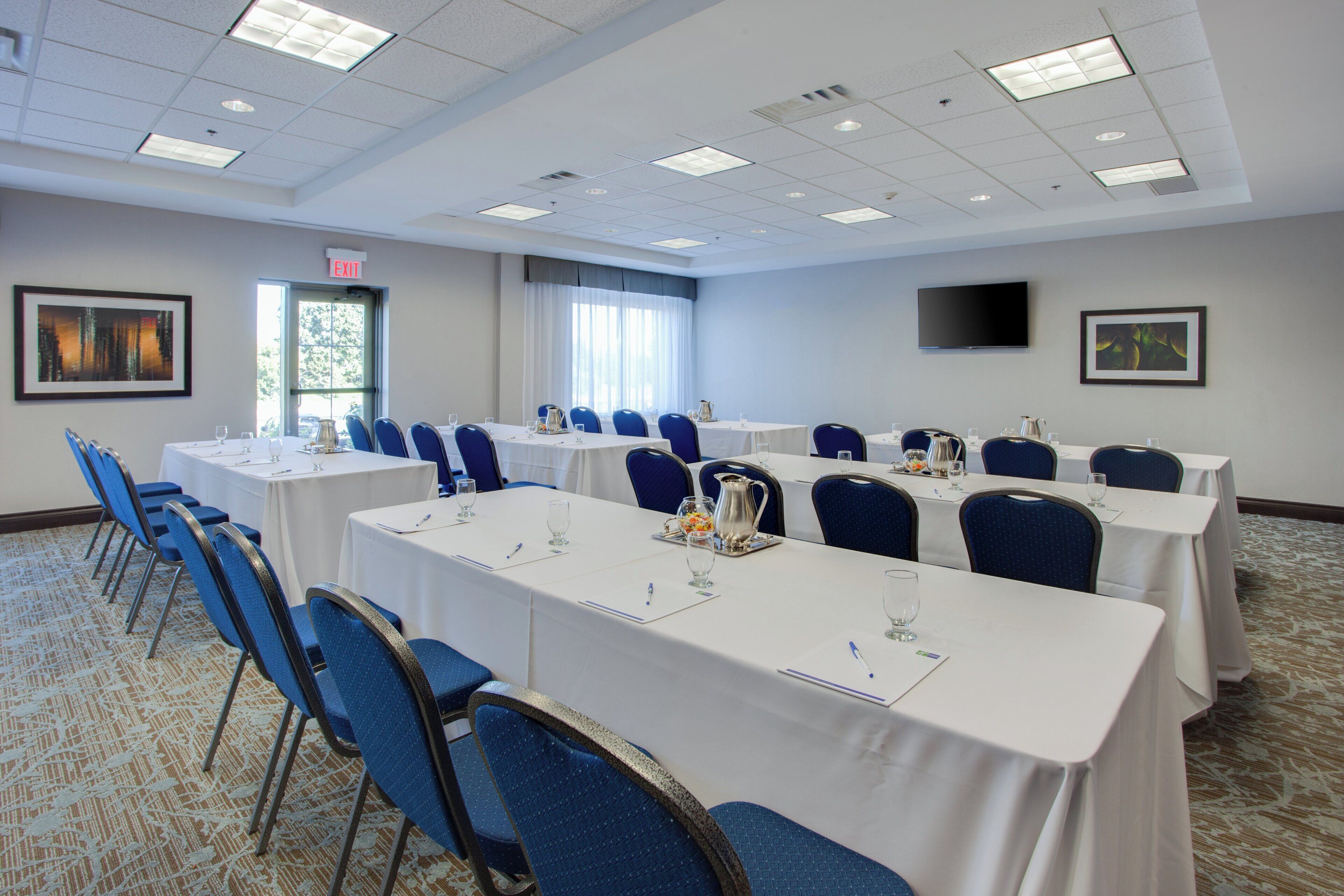 A conference room with multiple tables and chairs, a flat-screen TV mounted on the wall, and an exit sign.