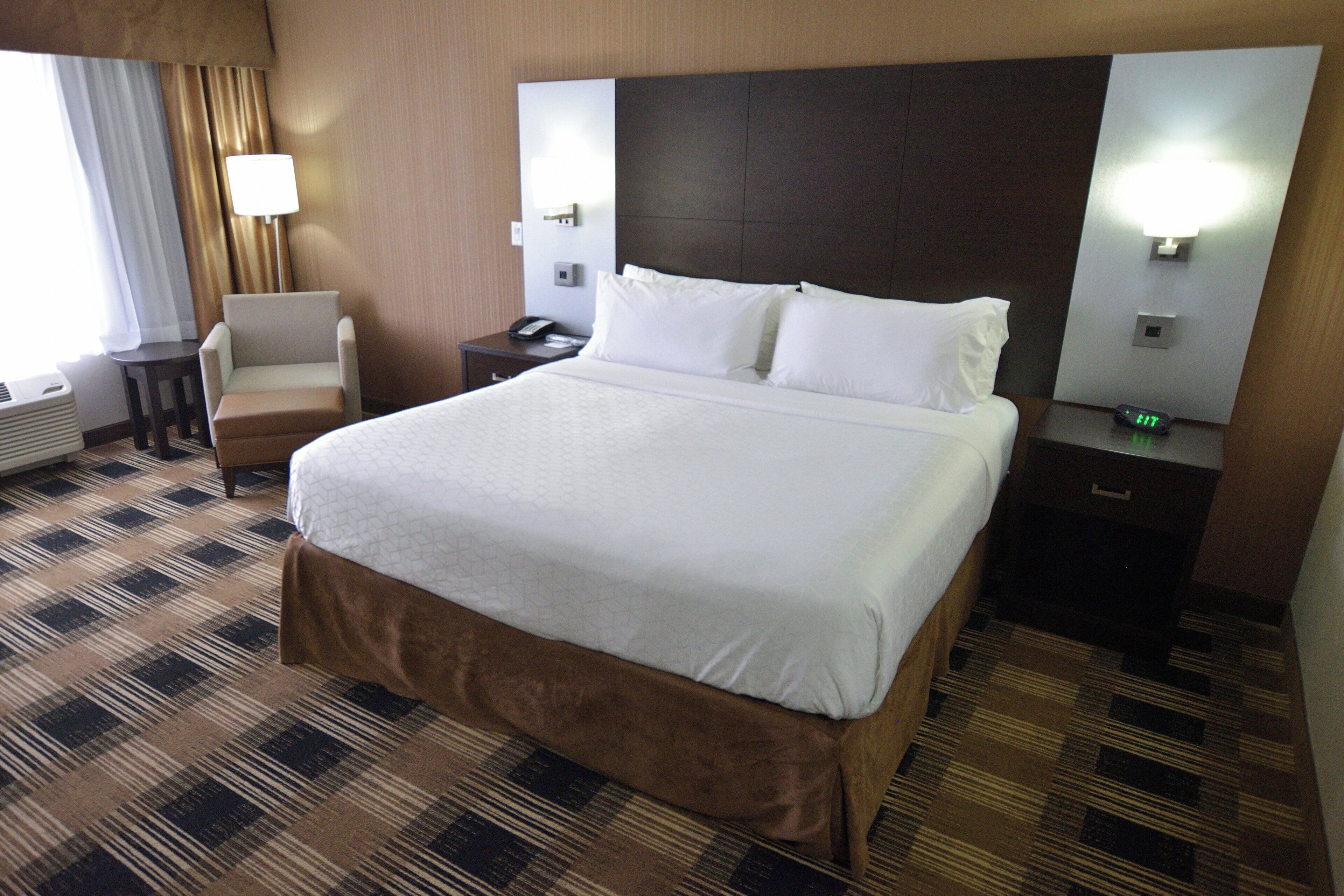 A hotel room with a large bed, a chair, a nightstand with a phone, and a wall-mounted light.