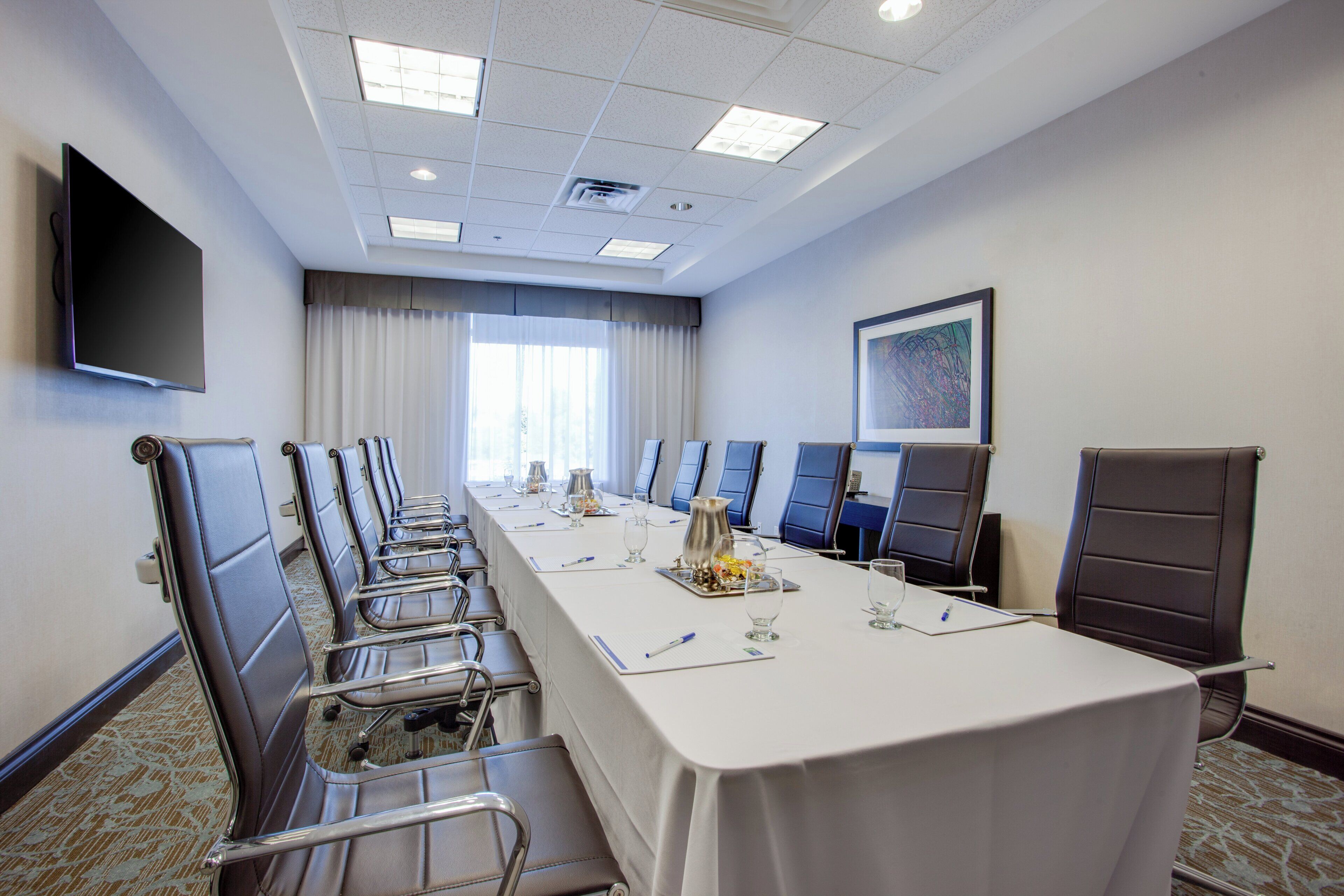 A conference room with a long table, chairs, a television, and a painting on the wall.