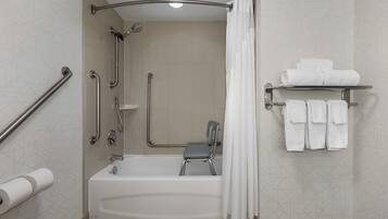 A modern bathroom with a walk-in shower, grab bars, a shower chair, and a towel rack with towels.
