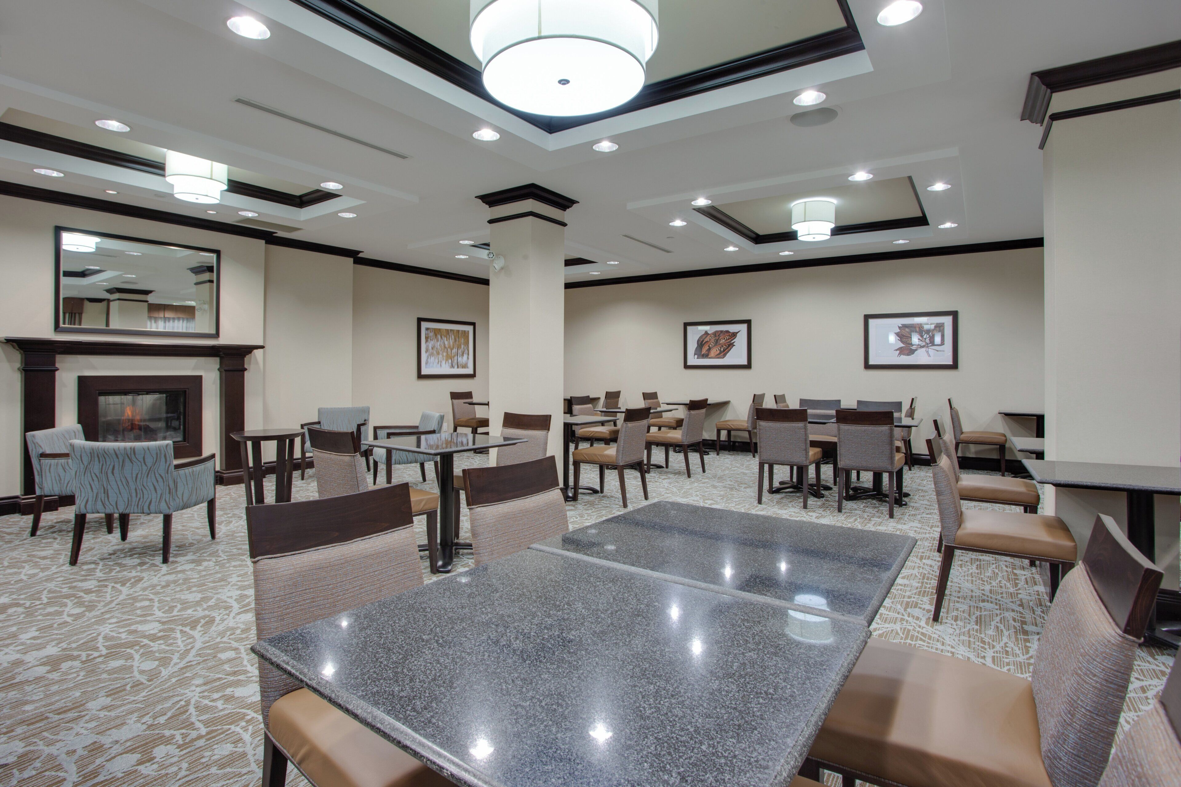 A hotel dining area with multiple tables and chairs, a fireplace, and framed artwork on the walls.