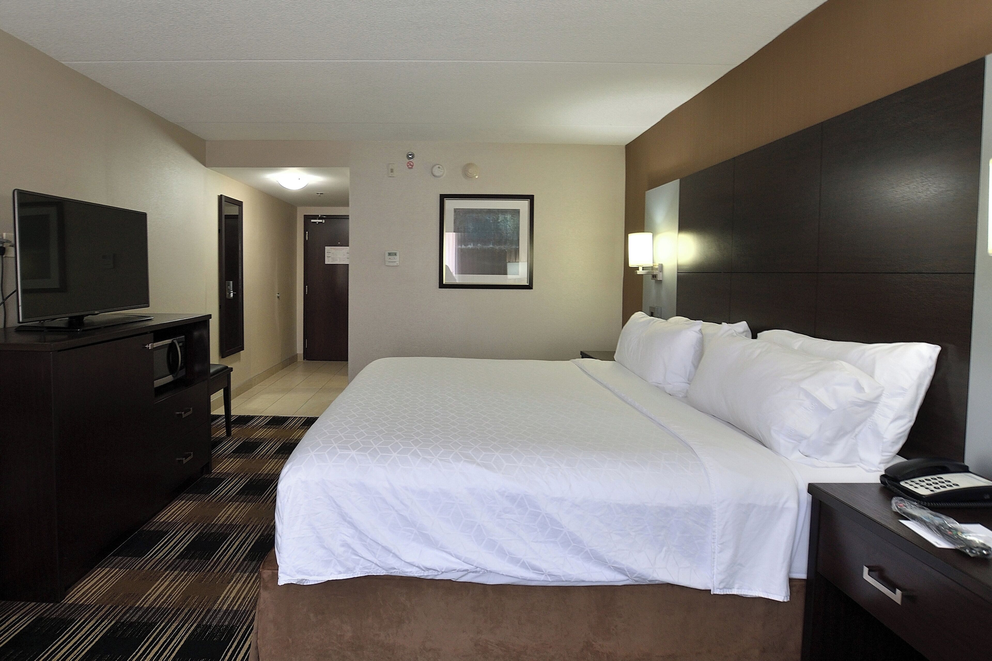 A hotel room with a bed, a television, a desk with a phone, and a door.