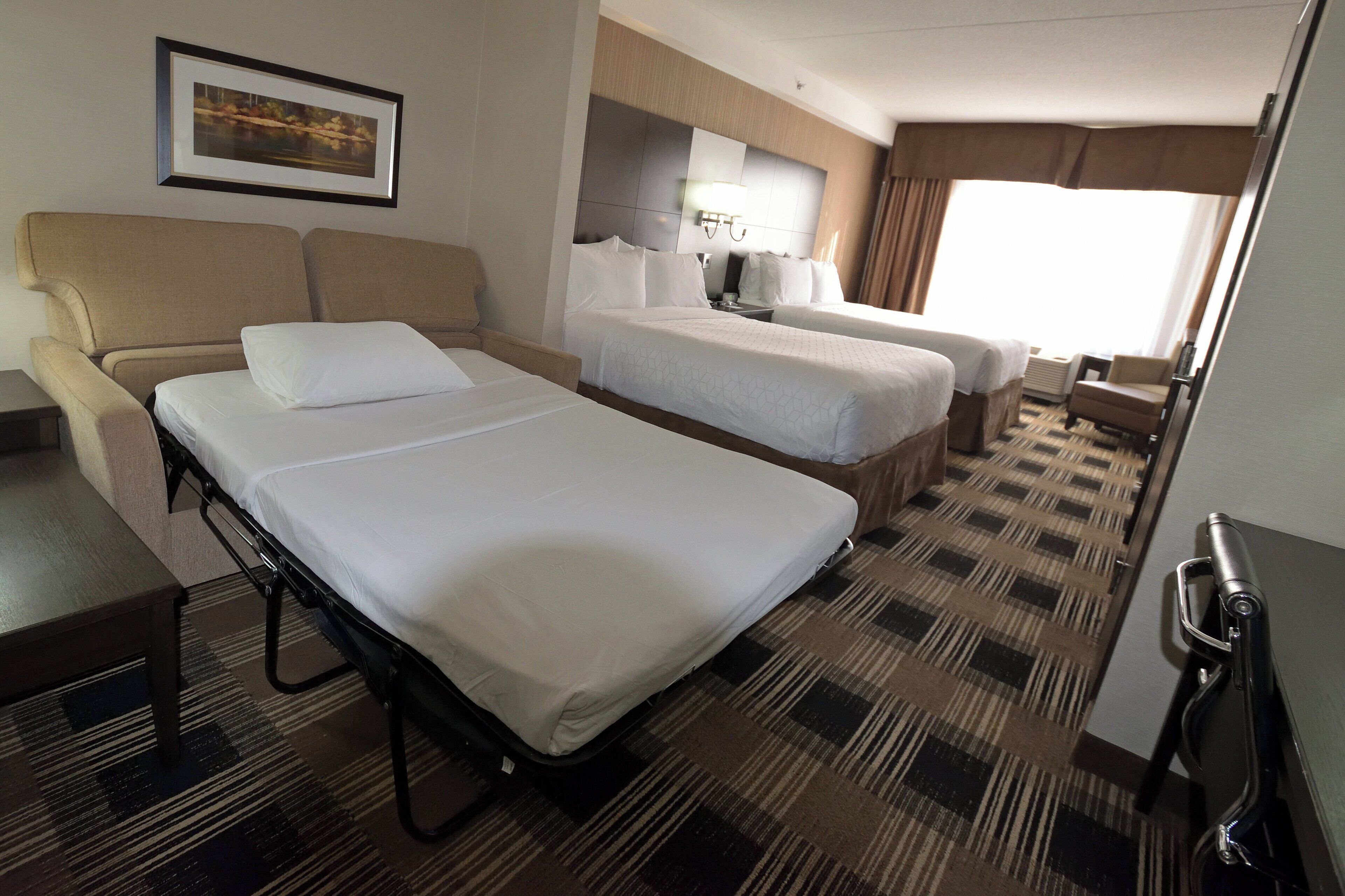 A hotel room with a bed, a sofa, a desk, and a window with curtains.