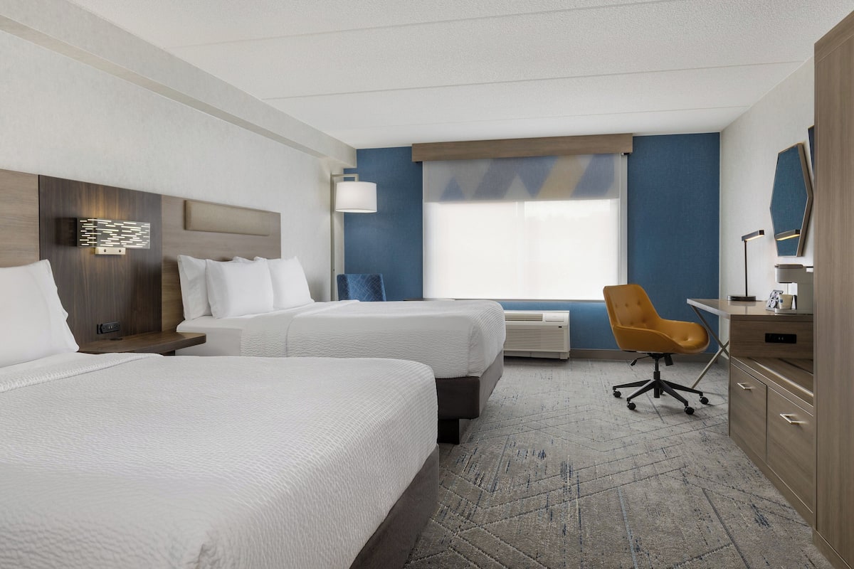 A hotel room with two beds, a desk, a chair, and a large window.