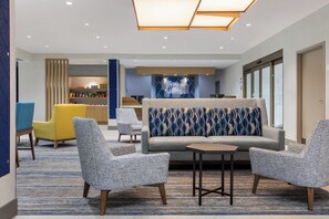 A modern lobby with a sofa, armchairs, a small table, and a snack bar.