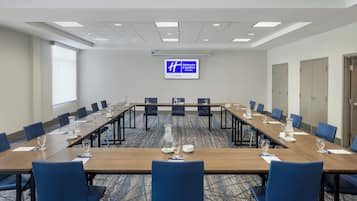 Une salle de conférence avec une longue table, des chaises bleues et un panneau « Holiday Inn Express » accroché au mur.