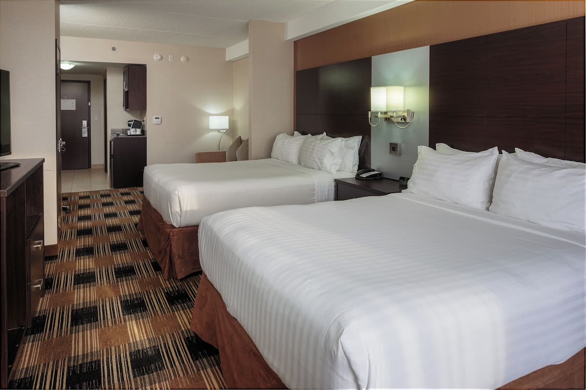 Two single beds with white duvets, a desk, and a kitchenette area with a refrigerator and coffee maker.