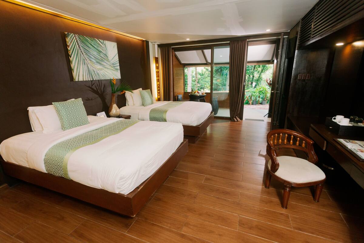 A hotel room with two beds, a wooden floor, a dining table with chairs, and a TV.