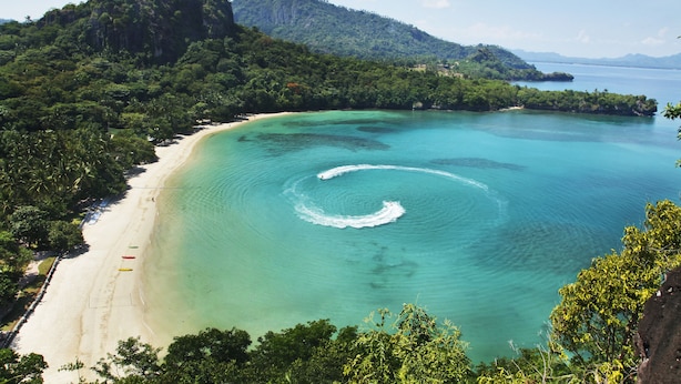 Uma praia com águas turquesa cristalinas, areia dourada e vegetação exuberante.