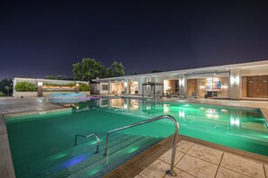 Una piscina con superficie de agua cristalina, rodeada por una zona techada con sillones de descanso y una barra.