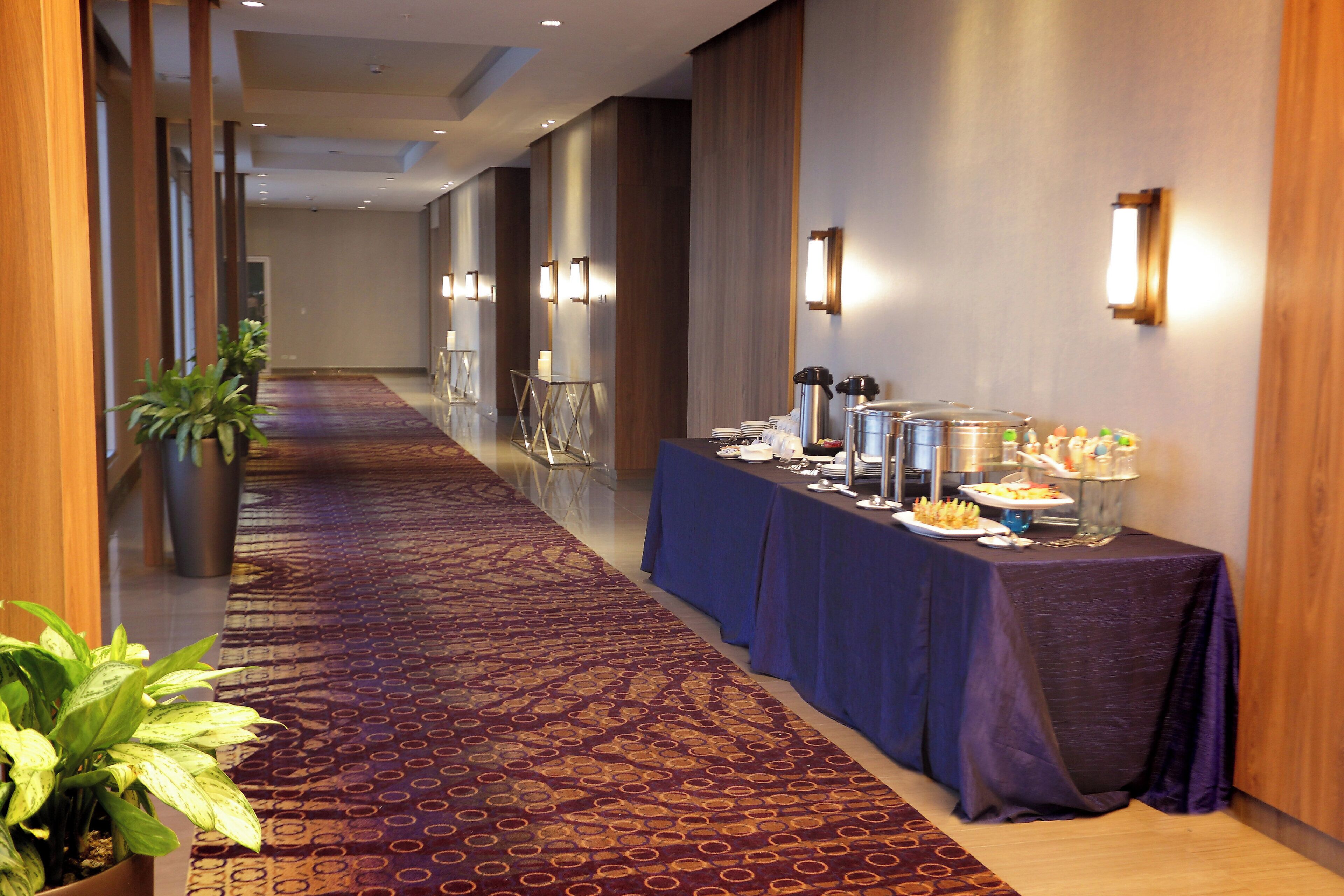 Un couloir d’hôtel avec une table de buffet, des plantes en pot et un tapis à motifs.