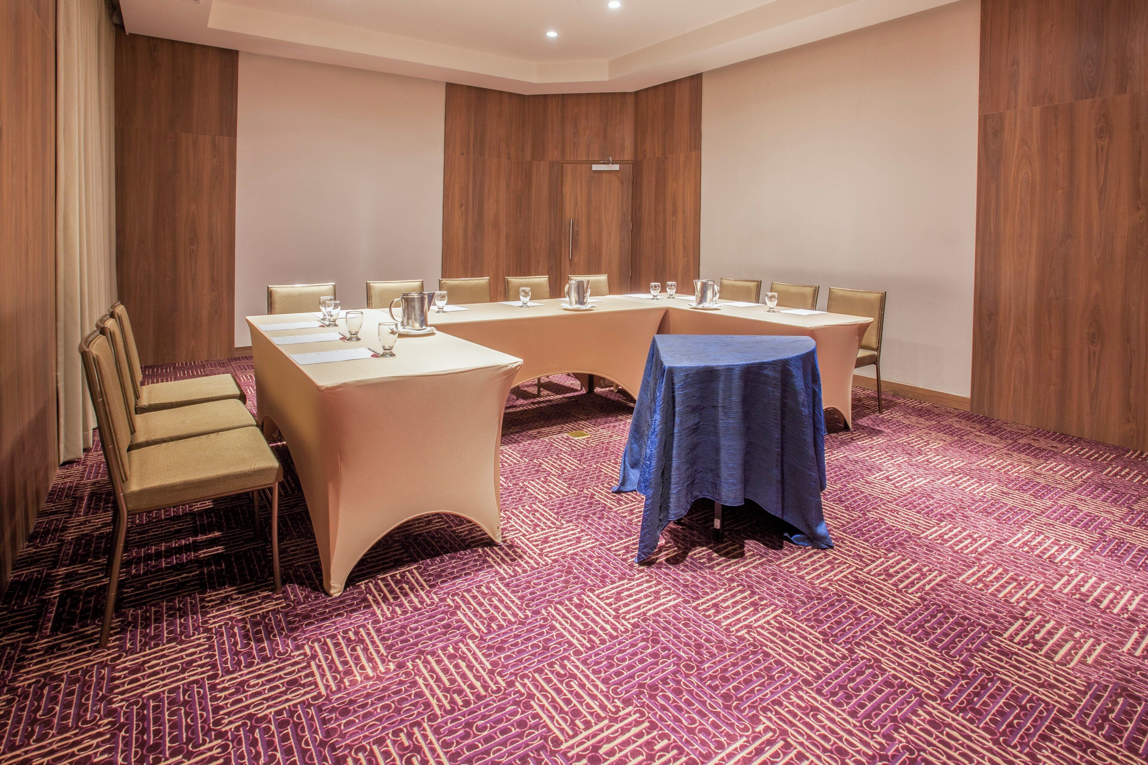A conference room with a long table, chairs, and a smaller table covered with a blue cloth.