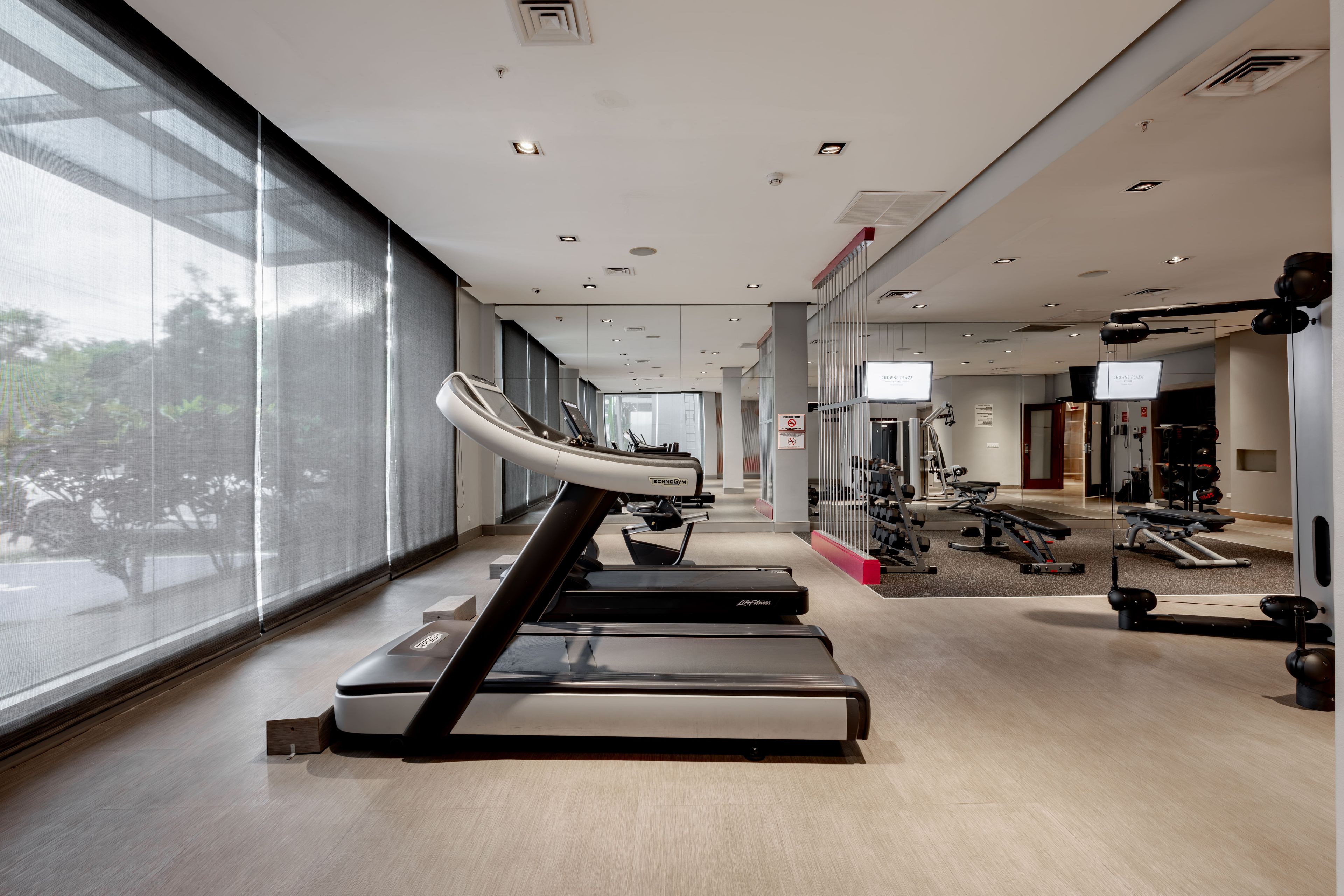 Ein modernes Fitnessstudio mit Laufbändern, Krafttrainingsgeräten und einem großen Fenster mit Tageslicht.