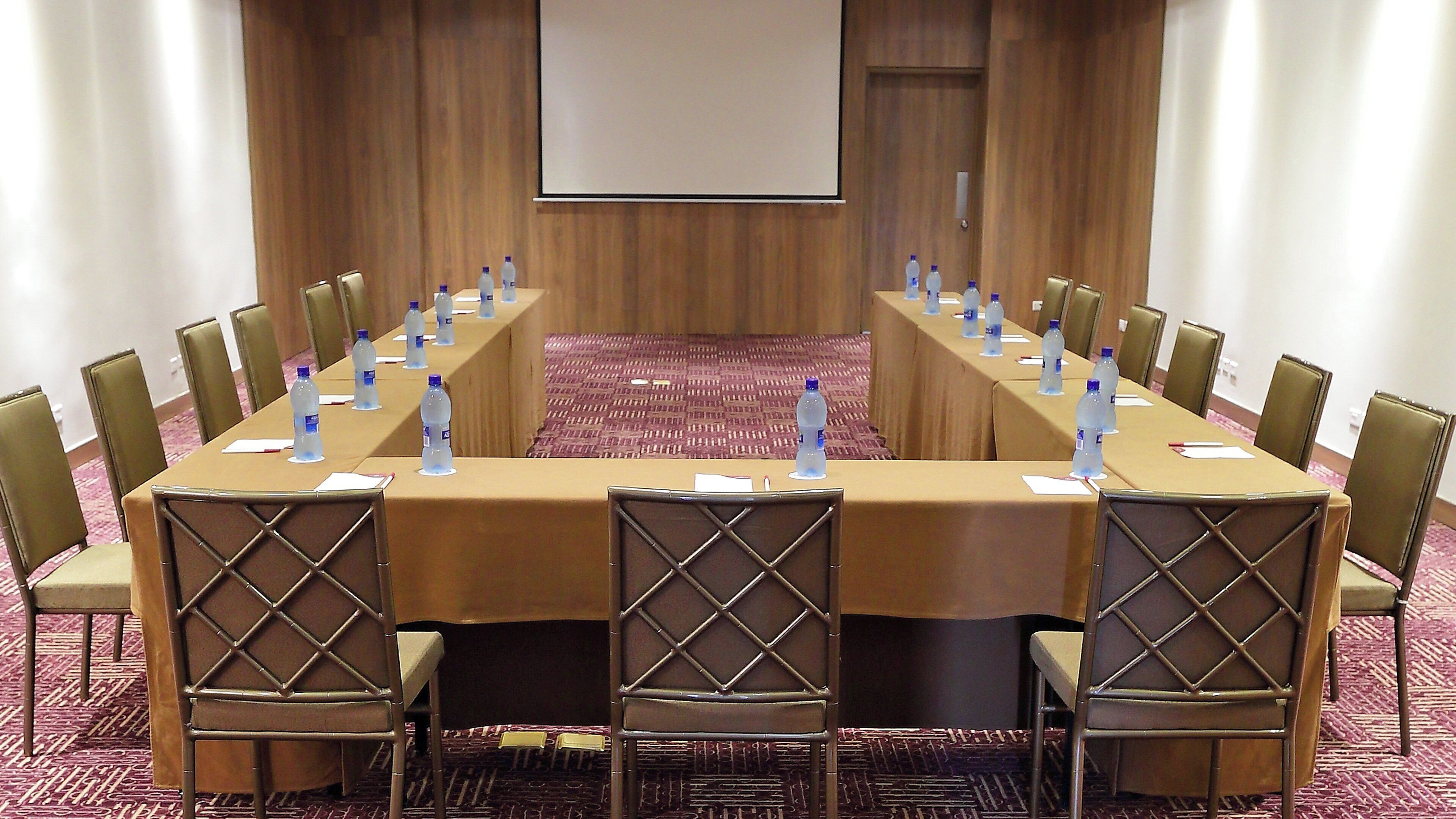 A conference room with a long table, chairs, water bottles, and a projector screen.