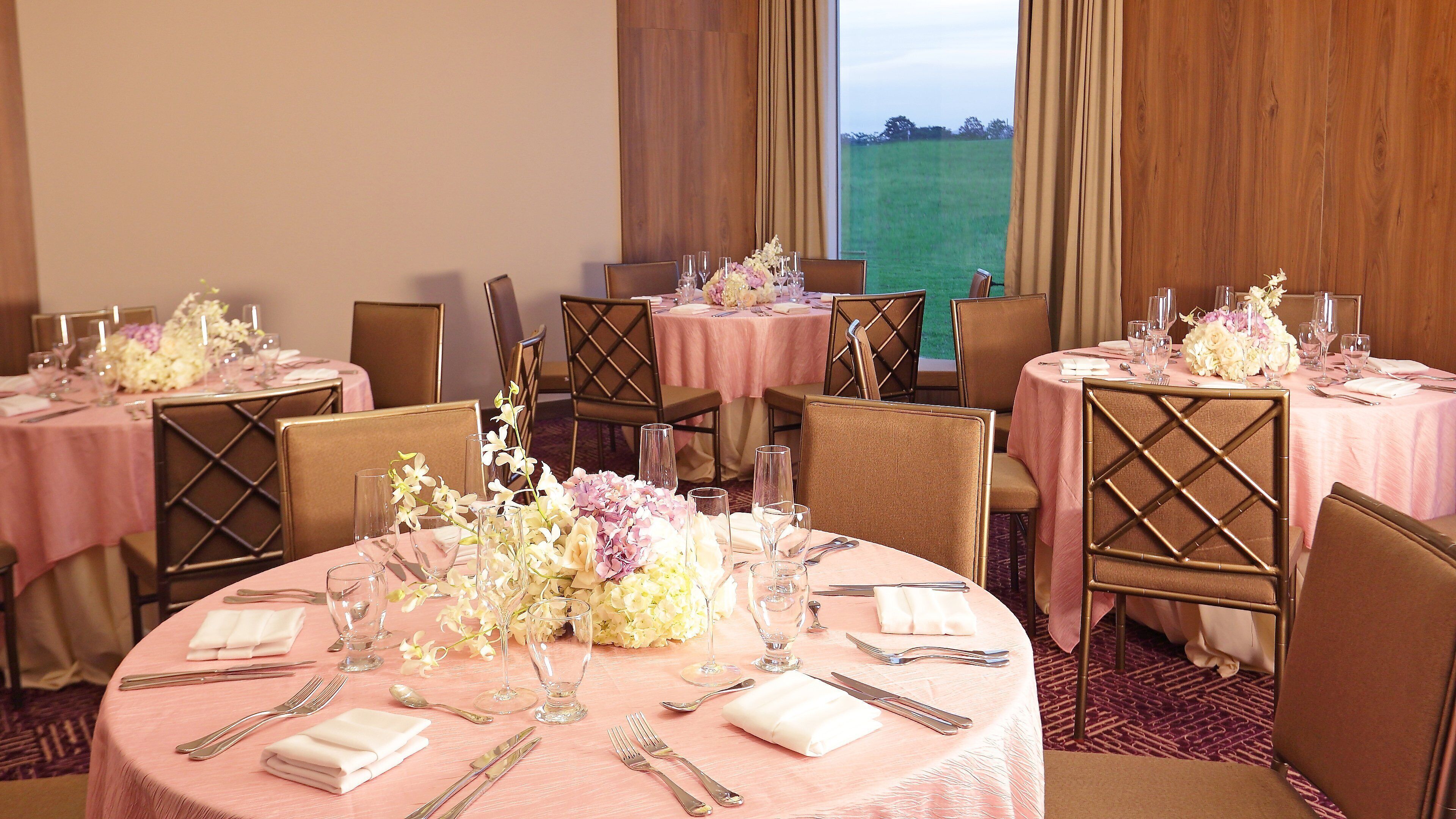 Un espace repas avec des tables rondes disposées pour accueillir quatre personnes, chacune étant recouverte d’une nappe rose, agrémentée de serviettes blanches et d’un centre de table floral.
