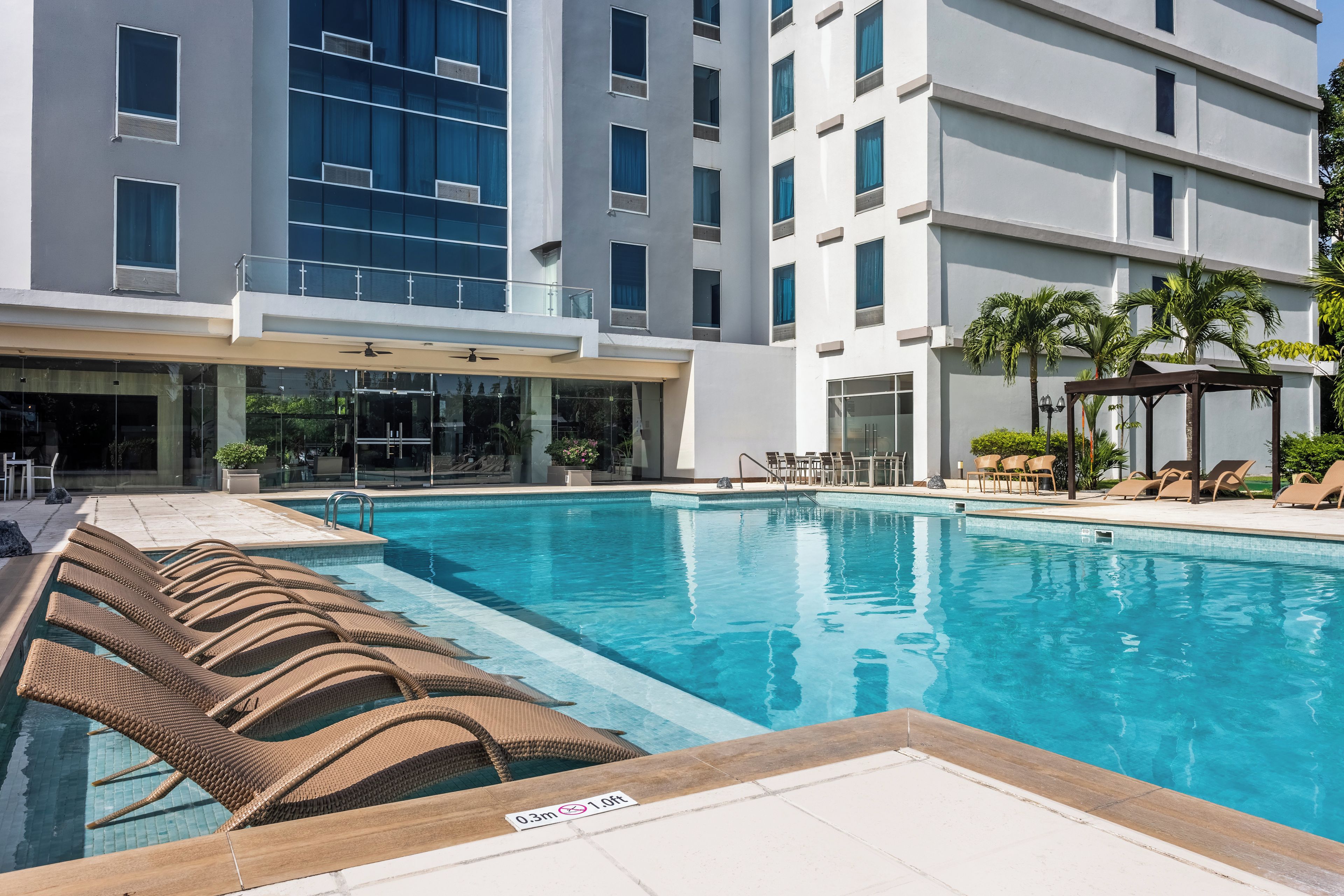 A swimming pool with lounge chairs and a building with multiple windows and balconies.