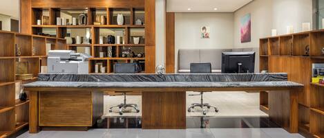 A modern office with a large marble desk, wooden shelving, and a grey couch.