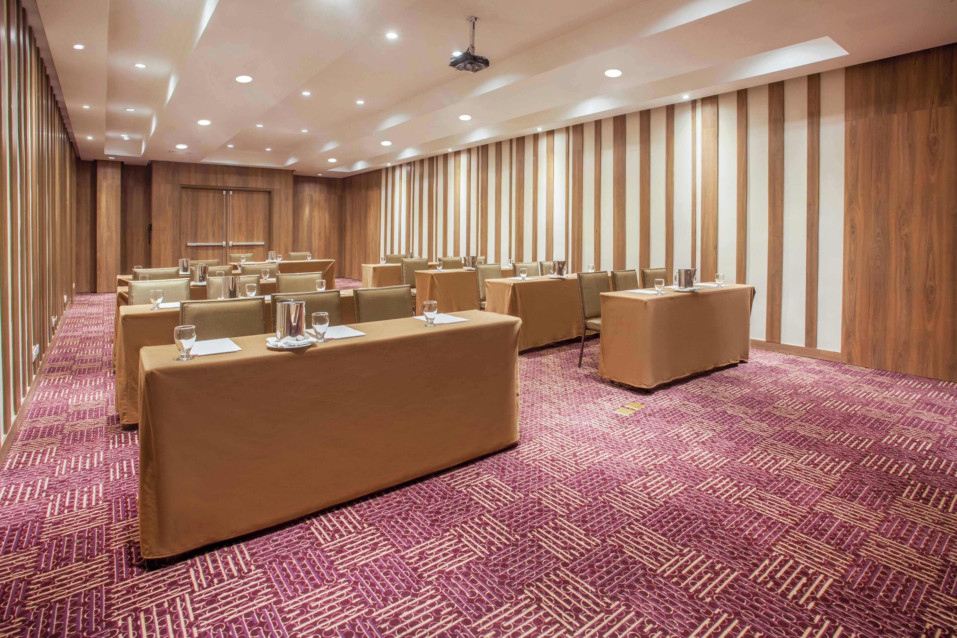 Un salón de conferencias con varias mesas, sillas y piso alfombrado.