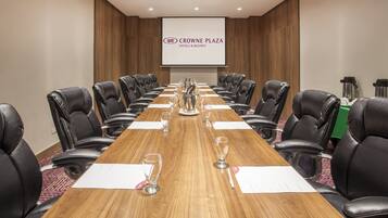 A conference room with a long wooden table, black leather chairs, and a projector screen displaying "Crowne Plaza Hotels & Resorts".
