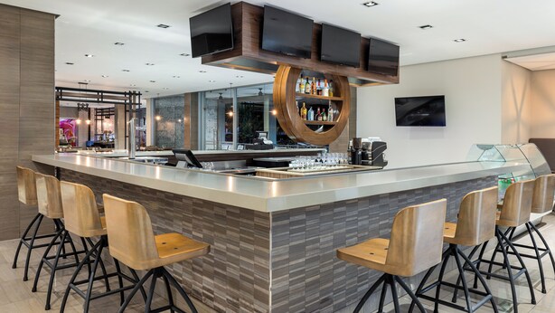 Un área de bar moderna con una isla central, taburetes y una televisión montada en el techo.