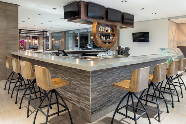Un área de bar moderna con una isla central, taburetes y una televisión montada en el techo.
