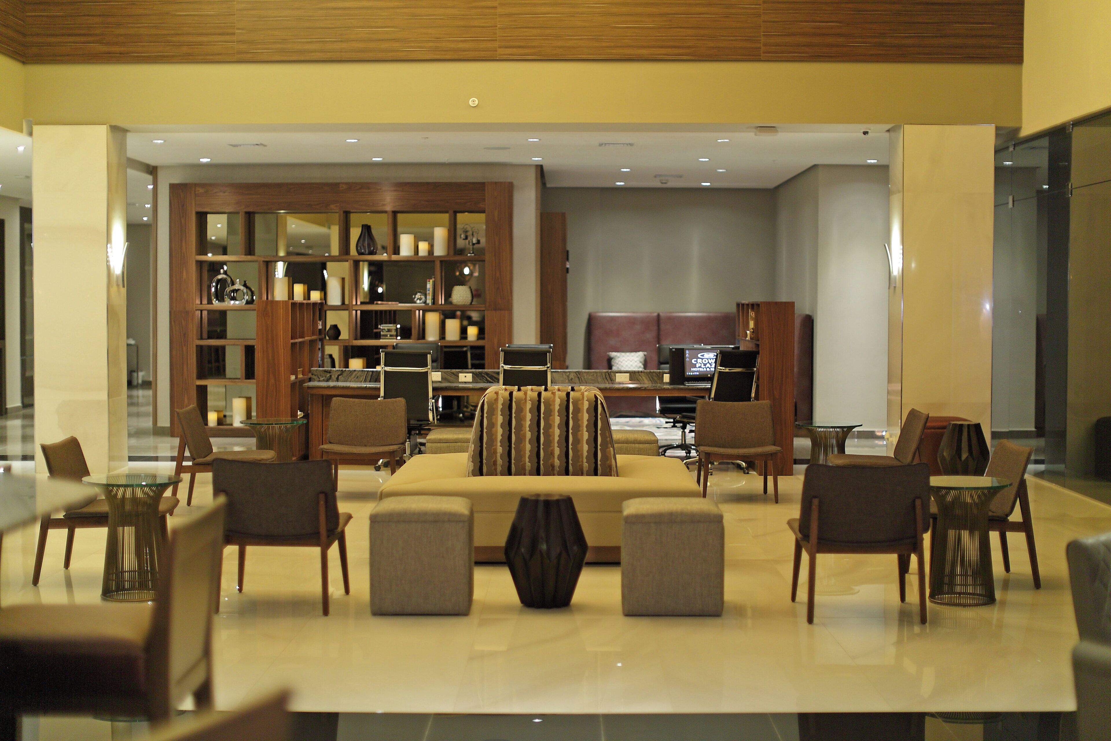 A modern hotel lobby with a seating area, a reception desk, and a large bookshelf.