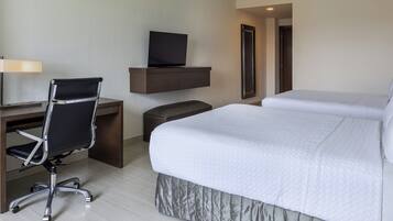 A hotel room with a bed, a desk with a chair, a television on a shelf, and a mirror.