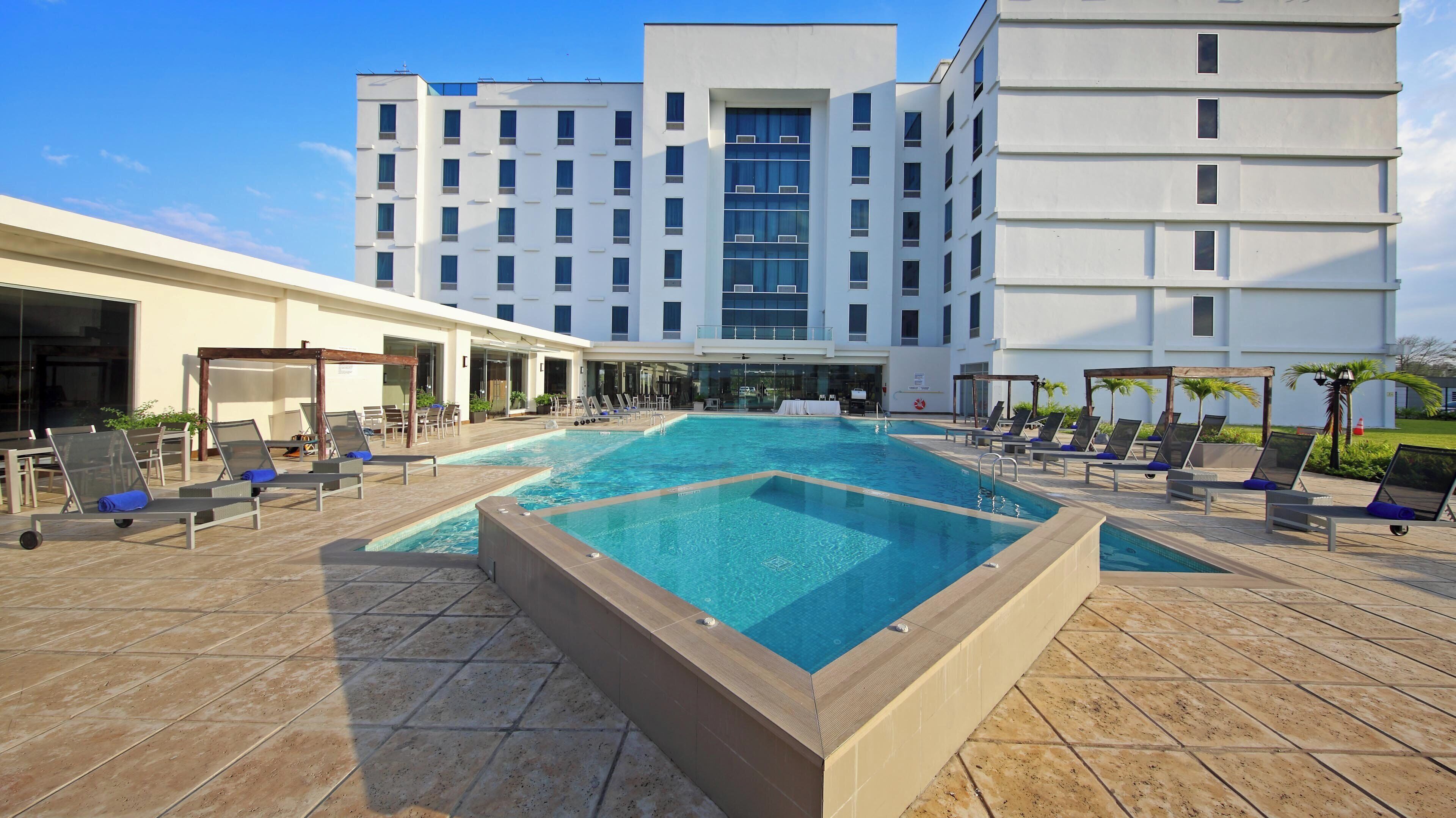 A hotel pool area with multiple lounge chairs and a large rectangular pool.
