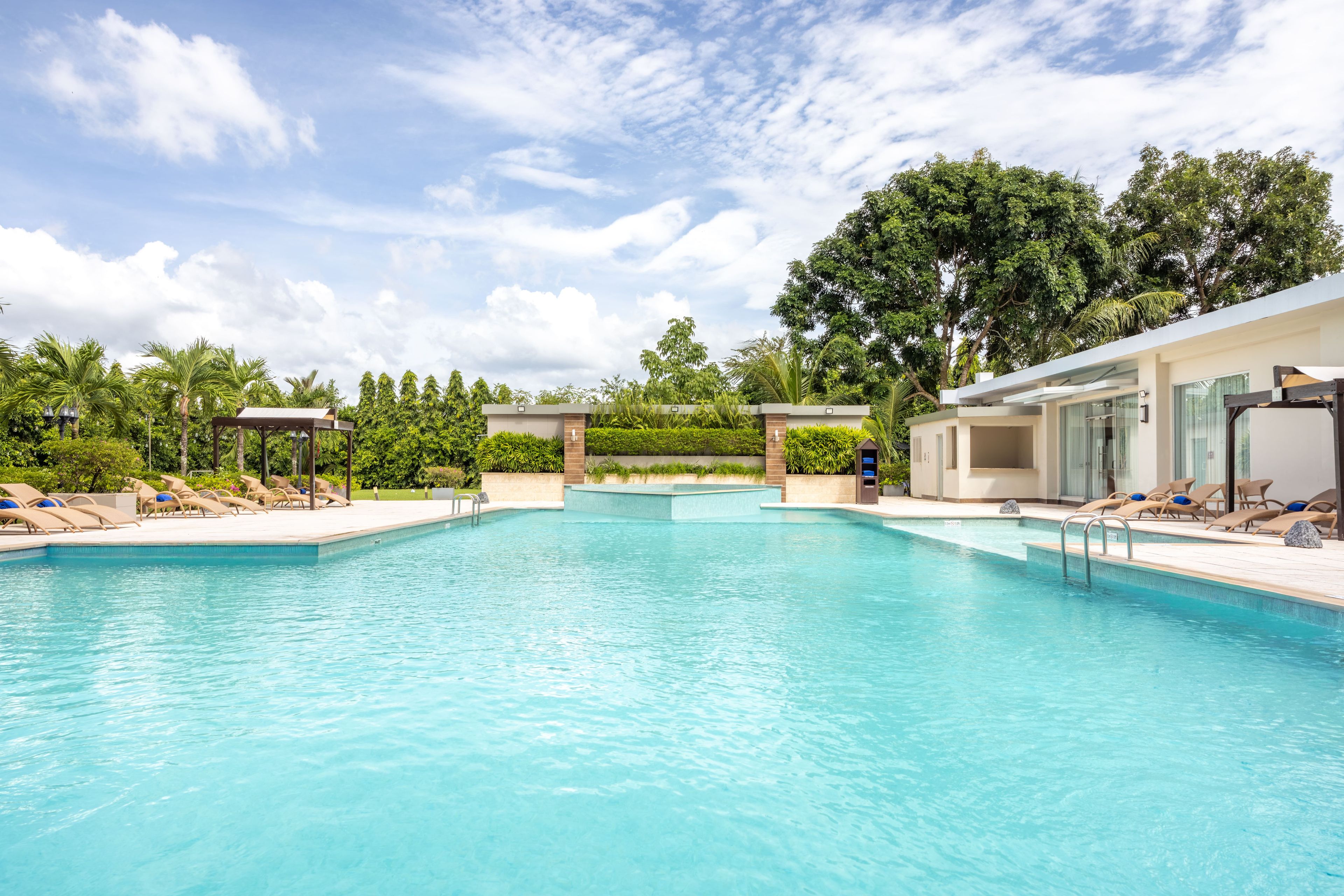 Una piscina con sillas de descanso y un edificio con amplios ventanales.