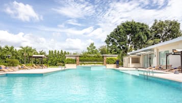 Una piscina con sillas de descanso y un edificio con amplios ventanales.